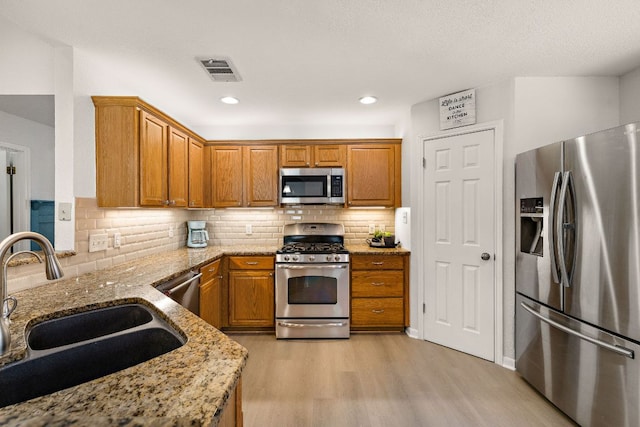 2104 Faldo Ln, Round Rock, TX 78664 - kitchen featuring appliances with stainless steel finishes, a sink, light wood finished floors, light stone counters, and brown cabinets