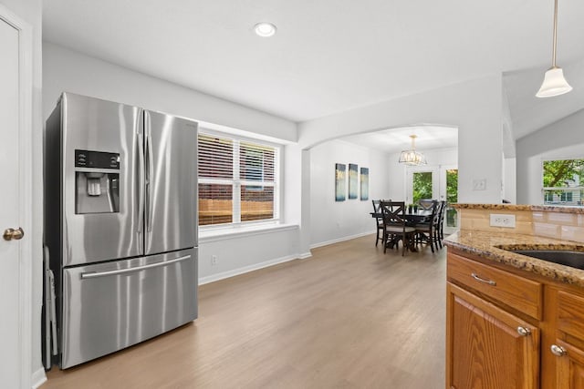 2104 Faldo Ln, Round Rock, TX 78664 - kitchen with stainless steel refrigerator with ice dispenser, arched walkways, brown cabinets, light wood-type flooring, and light stone counters
