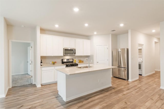 kitchen featuring appliances with stainless steel finishes, an island with sink, a sink, and light wood-style flooring