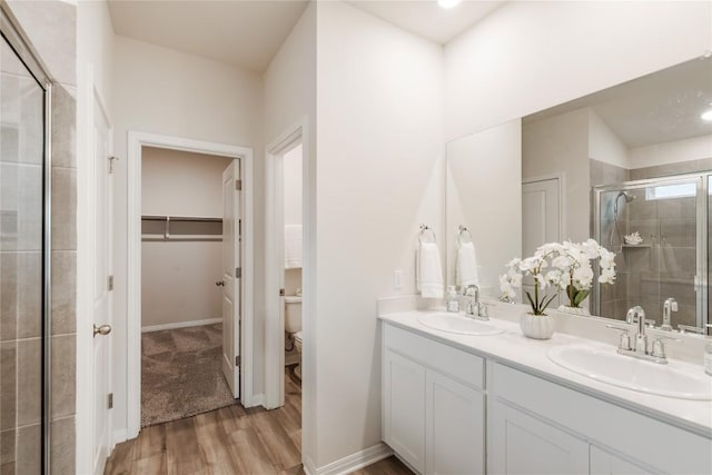 bathroom with wood finished floors, a sink, a stall shower, and toilet