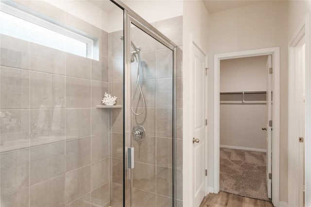 full bath featuring a walk in closet, wood finished floors, and a shower stall