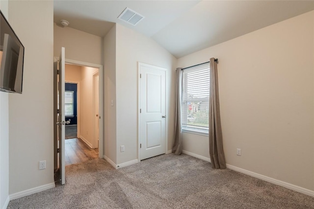 unfurnished bedroom featuring baseboards, visible vents, lofted ceiling, and carpet