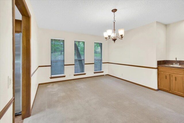 empty room featuring a textured ceiling, an inviting chandelier, light carpet, and a sink