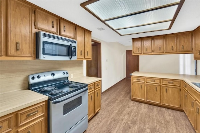 kitchen featuring baseboards, light wood-type flooring, light countertops, brown cabinets, and stainless steel appliances