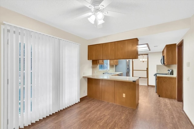 kitchen featuring brown cabinetry, a peninsula, wood finished floors, range with electric stovetop, and light countertops