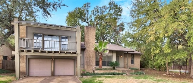 view of front of property featuring driveway, a chimney, a garage, brick siding, and a balcony