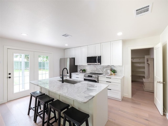 kitchen featuring visible vents, a breakfast bar, light wood-style floors, a sink, and appliances with stainless steel finishes