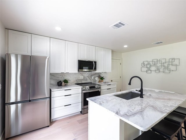 11224 Pickard Ln, Austin, TX 78748 - kitchen featuring appliances with stainless steel finishes, white cabinetry, light wood-style flooring, light stone countertops, and decorative backsplash