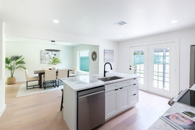 kitchen with light stone counters, a sink, light wood finished floors, stainless steel dishwasher, and visible vents