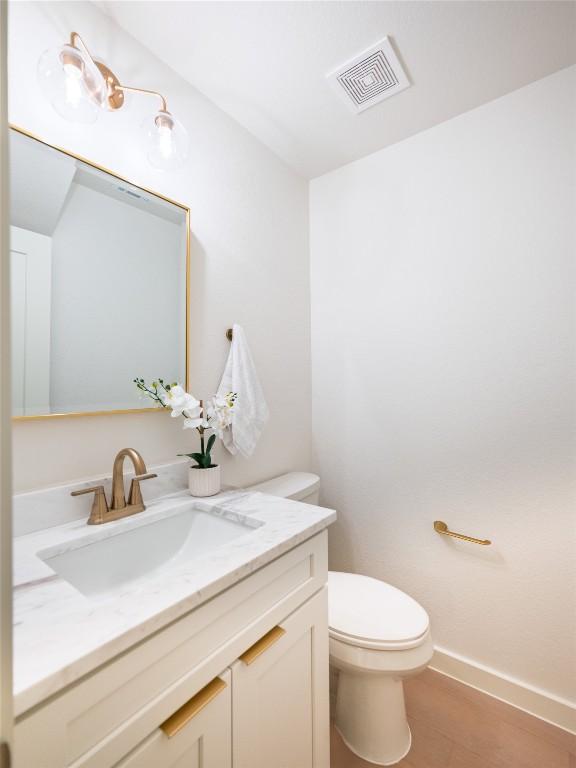 bathroom featuring visible vents, wood finished floors, vanity, baseboards, and toilet