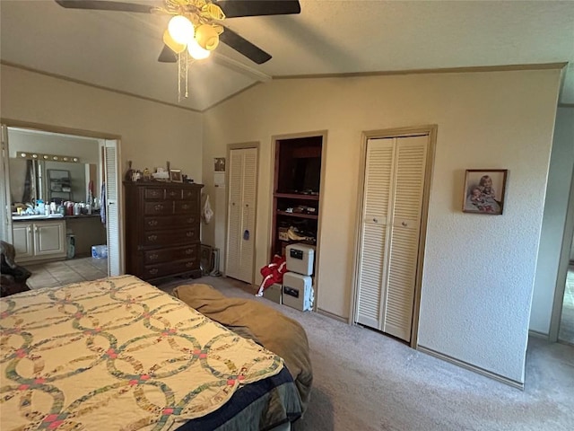 bedroom featuring lofted ceiling, two closets, light carpet, ceiling fan, and connected bathroom