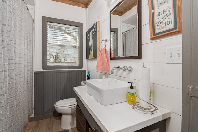 full bathroom featuring curtained shower, wood finished floors, a wainscoted wall, vanity, and toilet