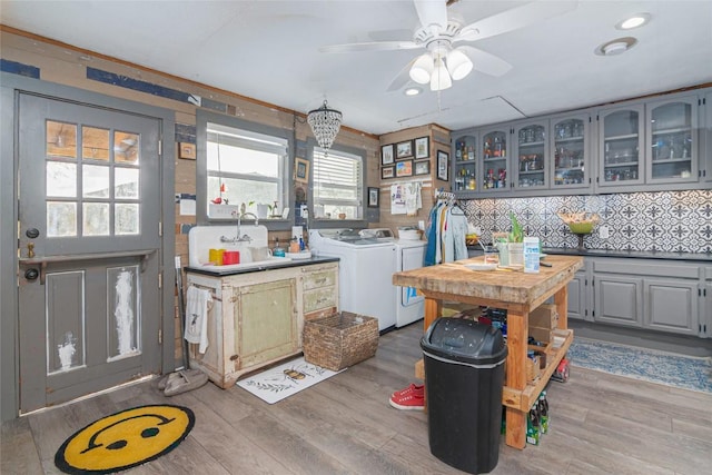 kitchen with a ceiling fan, washing machine and clothes dryer, light wood-type flooring, a sink, and glass insert cabinets