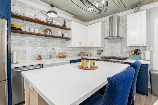 kitchen featuring wall chimney range hood, appliances with stainless steel finishes, a sink, light countertops, and a kitchen breakfast bar