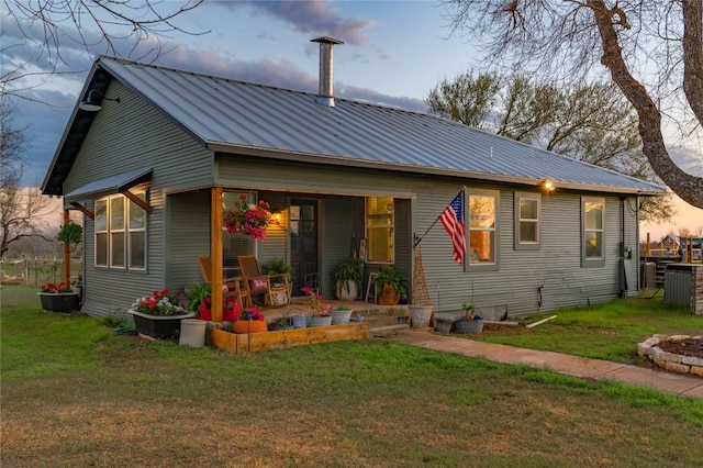 back of house at dusk with covered porch, central air condition unit, a yard, and metal roof