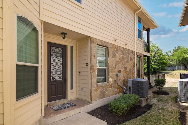 property entrance featuring fence, central AC, and stone siding