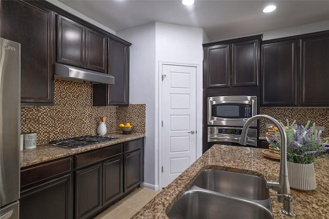 kitchen featuring appliances with stainless steel finishes, tasteful backsplash, a sink, dark stone counters, and under cabinet range hood
