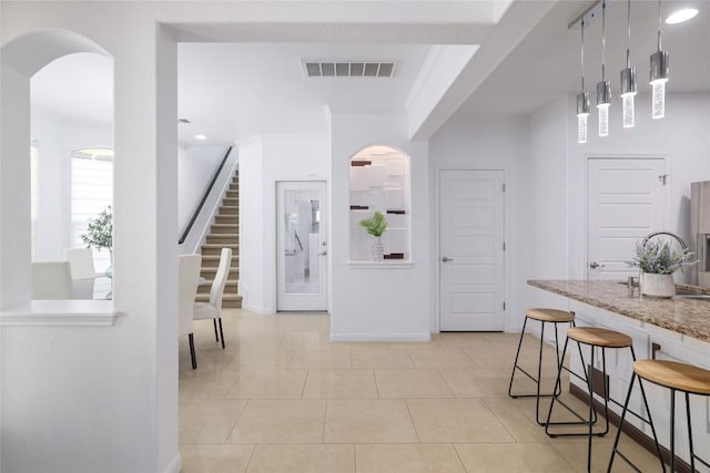 interior space featuring visible vents, arched walkways, stairway, baseboards, and light tile patterned floors