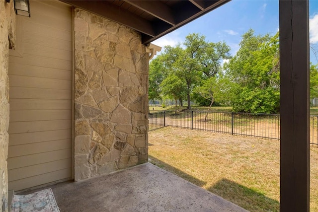 exterior space featuring a lawn, fence, stone siding, and a patio