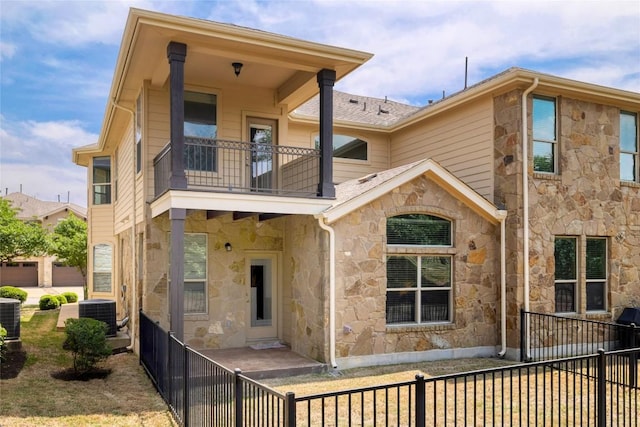 rear view of house featuring central air condition unit, a fenced backyard, a balcony, and stone siding