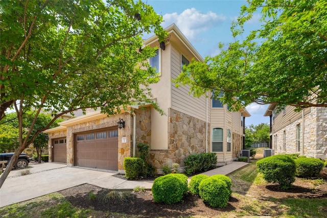 view of home's exterior featuring cooling unit, driveway, stone siding, and a garage