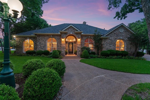 view of front of home featuring a lawn, brick siding, roof with shingles, and a chimney