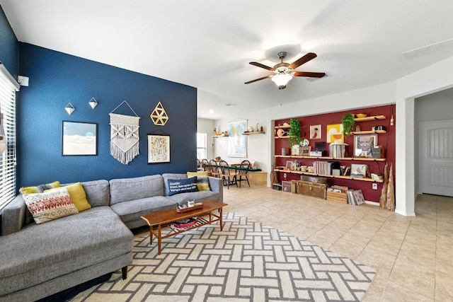 living area featuring tile patterned floors, ceiling fan, an accent wall, and visible vents