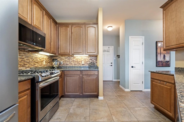 6006 Seville Dr, Austin, TX 78724 - kitchen with brown cabinetry, light tile patterned flooring, dark stone countertops, backsplash, and stainless steel appliances