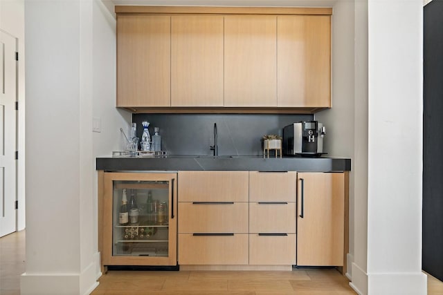 bar featuring baseboards, beverage cooler, indoor bar, a sink, and light wood finished floors