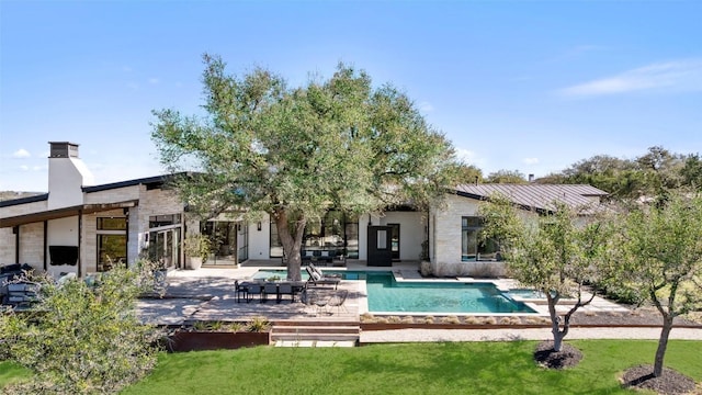 back of house with a standing seam roof, a lawn, an outdoor pool, a patio area, and stone siding