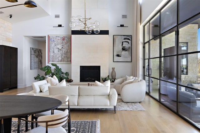 living room featuring visible vents, a towering ceiling, wood finished floors, a tile fireplace, and an inviting chandelier