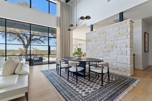 dining room featuring a healthy amount of sunlight, baseboards, wood finished floors, and a towering ceiling