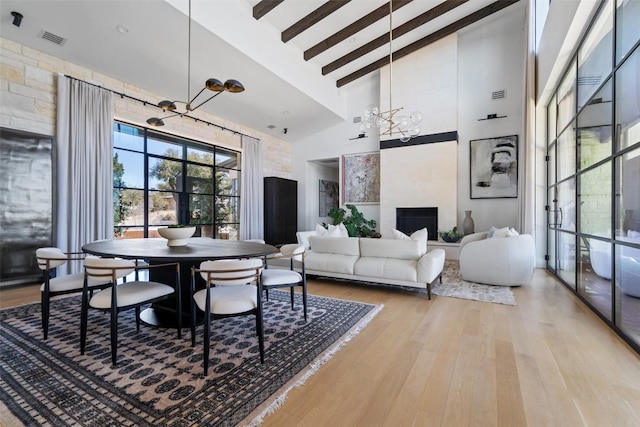 dining room with a notable chandelier, beam ceiling, high vaulted ceiling, light wood-type flooring, and visible vents