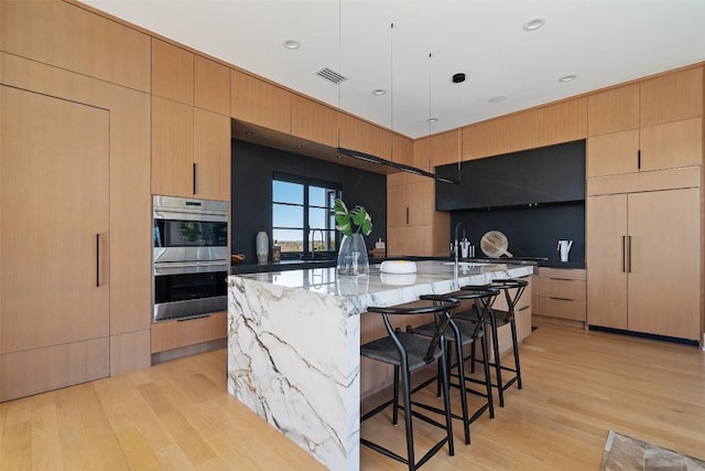 kitchen featuring double oven, a kitchen bar, a center island, light stone counters, and light wood finished floors