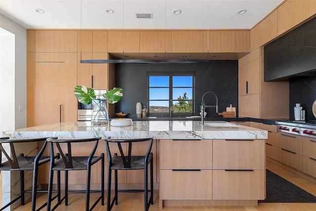 kitchen with light brown cabinetry, light stone countertops, a sink, stainless steel gas stovetop, and modern cabinets