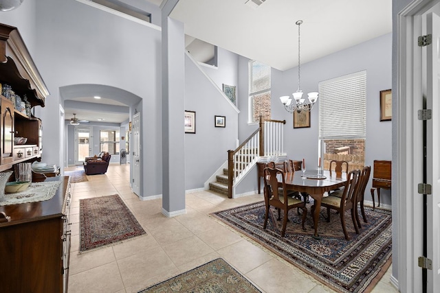 dining room featuring arched walkways, ceiling fan with notable chandelier, baseboards, light tile patterned floors, and stairway