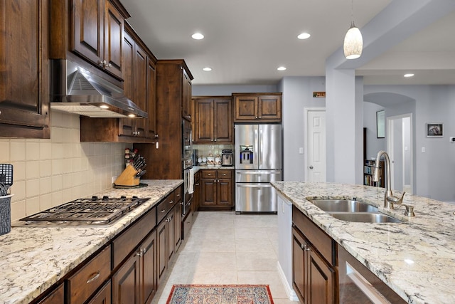 kitchen featuring appliances with stainless steel finishes, tasteful backsplash, arched walkways, a sink, and under cabinet range hood