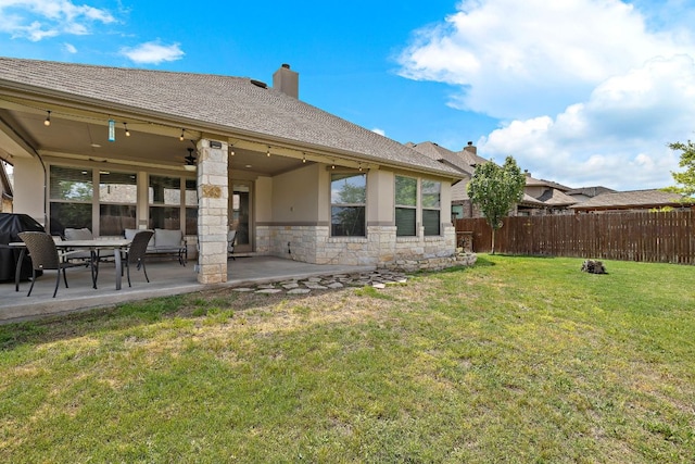 rear view of house featuring a chimney, a lawn, a patio area, fence, and stone siding