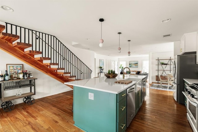 kitchen featuring light countertops, a kitchen island with sink, stainless steel appliances, open floor plan, and wood finished floors