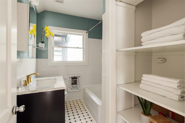 full bathroom featuring vanity, heating unit, toilet, tile walls, and a wainscoted wall