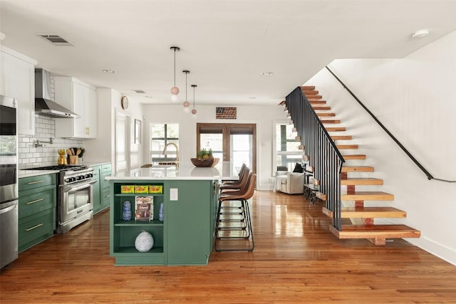 kitchen featuring wall chimney range hood, plenty of natural light, light countertops, green cabinetry, and high end range