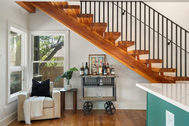 staircase featuring baseboards, wood finished floors, and a bar