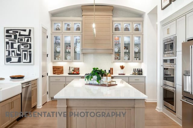 kitchen featuring a kitchen island, arched walkways, light wood finished floors, hanging light fixtures, and stainless steel appliances