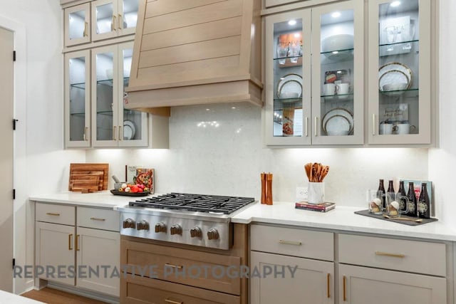kitchen featuring light stone countertops, stainless steel gas stovetop, backsplash, custom exhaust hood, and glass insert cabinets