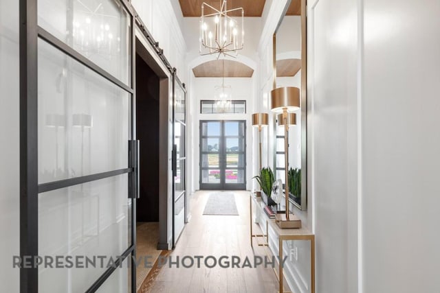 hallway featuring an inviting chandelier, a barn door, french doors, wood finished floors, and a towering ceiling
