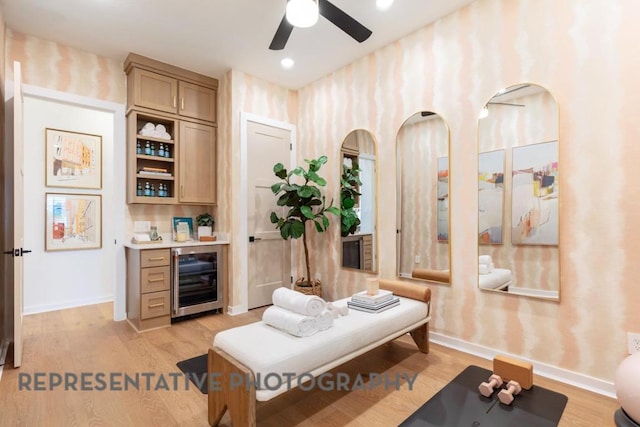 sitting room featuring wine cooler, baseboards, ceiling fan, and light wood-style floors