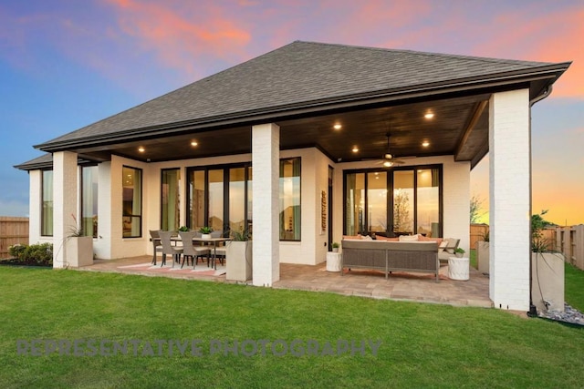 back of house at dusk with a shingled roof, a fenced backyard, an outdoor living space, a patio, and a yard