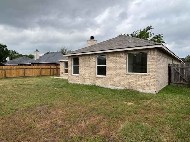 rear view of property with a lawn, a fenced backyard, roof with shingles, and a chimney