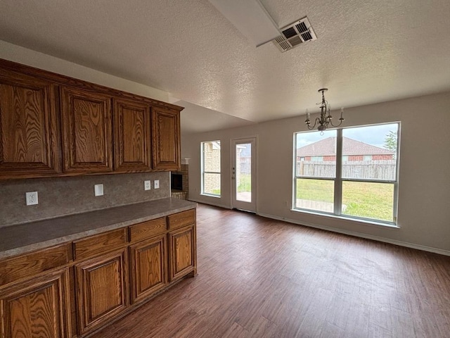kitchen featuring a notable chandelier, brown cabinetry, baseboards, visible vents, and dark wood-style floors