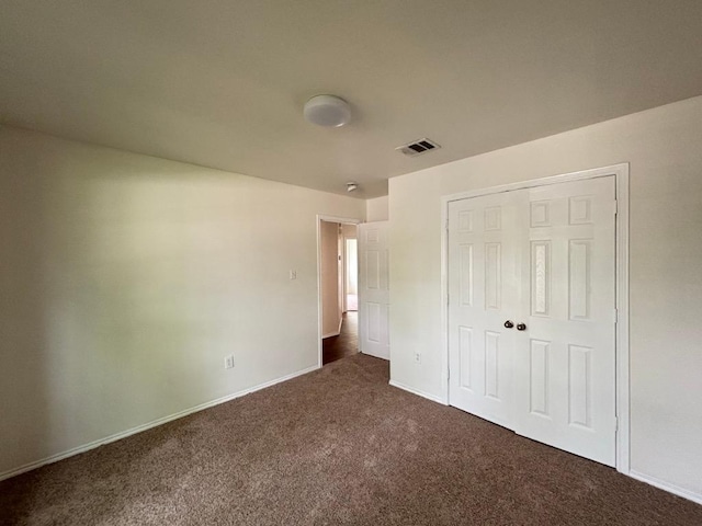 unfurnished bedroom featuring baseboards, visible vents, dark carpet, and a closet